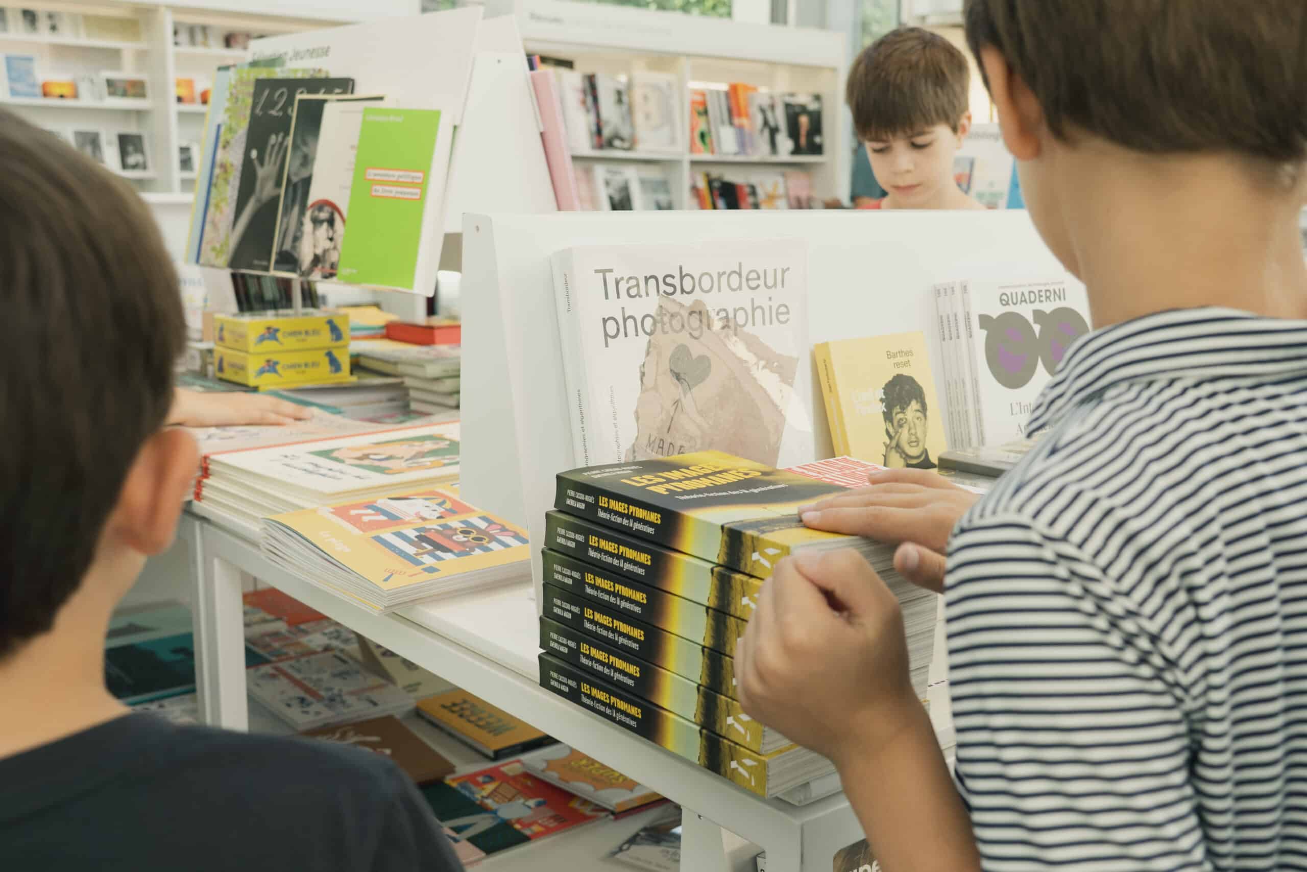 Plusieurs enfants consultent des livres dans la librairie du Jeu de Paume, devant des présentoirs remplis d'ouvrages.