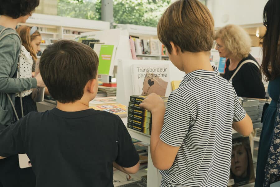 Plusieurs enfants consultent des livres dans la librairie du Jeu de Paume, devant des présentoirs remplis d'ouvrages.