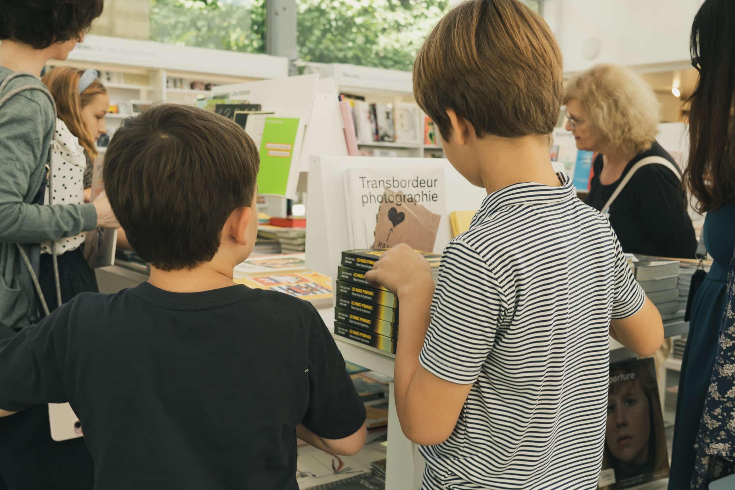 Plusieurs enfants consultent des livres dans la librairie du Jeu de Paume, devant des présentoirs remplis d'ouvrages.